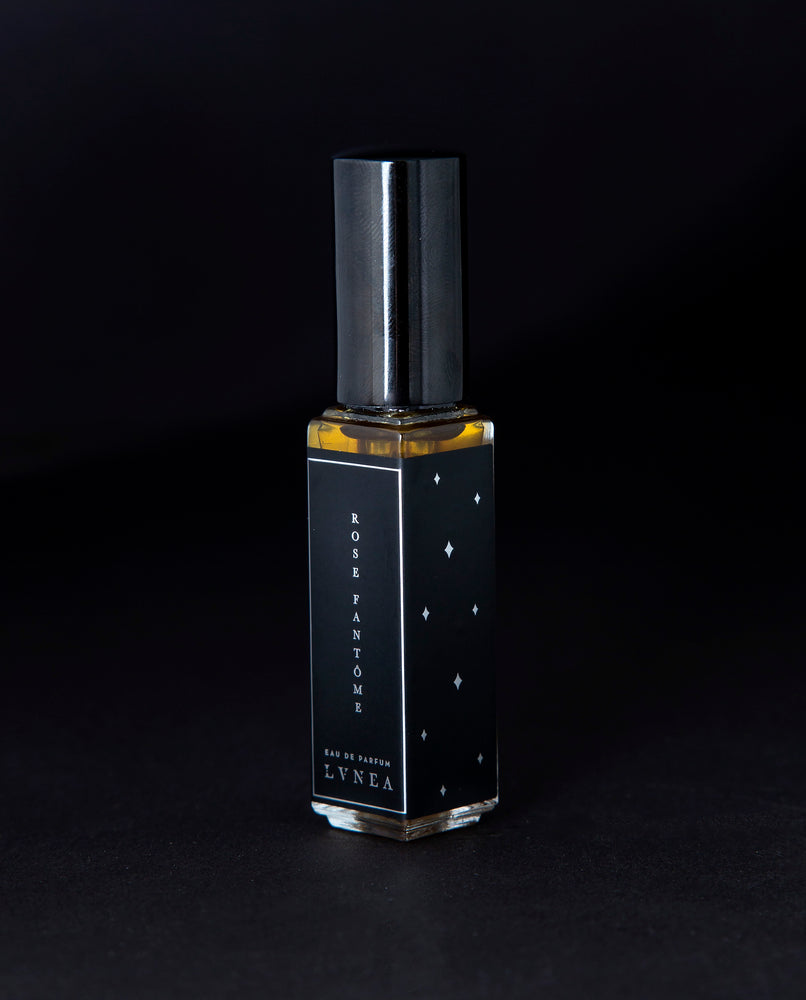 8ml clear glass bottle of LVNEA’s Rose Fantôme natural perfume on black background, bottle is rotated at a 3/4 angle exposing a star pattern on the label.