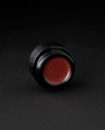 A deep, rosy blush coloured lip balm in a black glass pot on black background