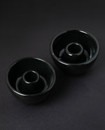 Two glossy black stoneware candle holders on black background, seen from 3/4 angle. 