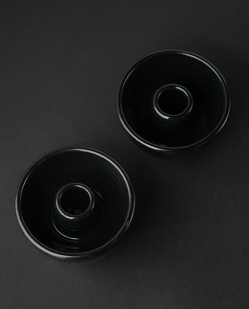 Two glossy black stoneware candle holders on black background, they are seen from an overhead angle.
