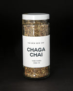 clear glass jar with white screw on cap and white label on black background. It contains The New New Age's "Chaga Chai" tea blend